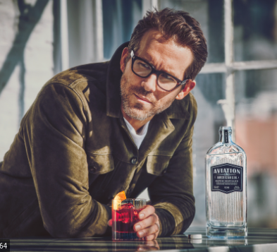 Ryan Reynolds leaning on a bar with a tumbler glass filled with Aviation Gin. Situated next to him is a bottle of Aviation Gin.
